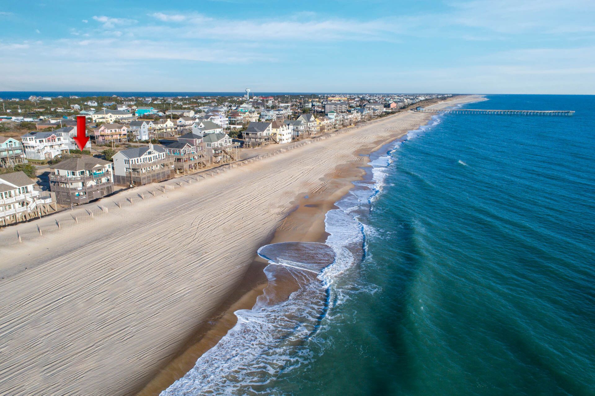 A coastal town with beachfront properties, a pier extending into the sea, and a clear sky.