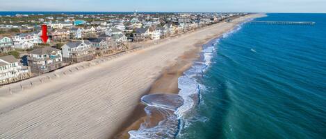 A coastal town with beachfront properties, a pier extending into the sea, and a clear sky.