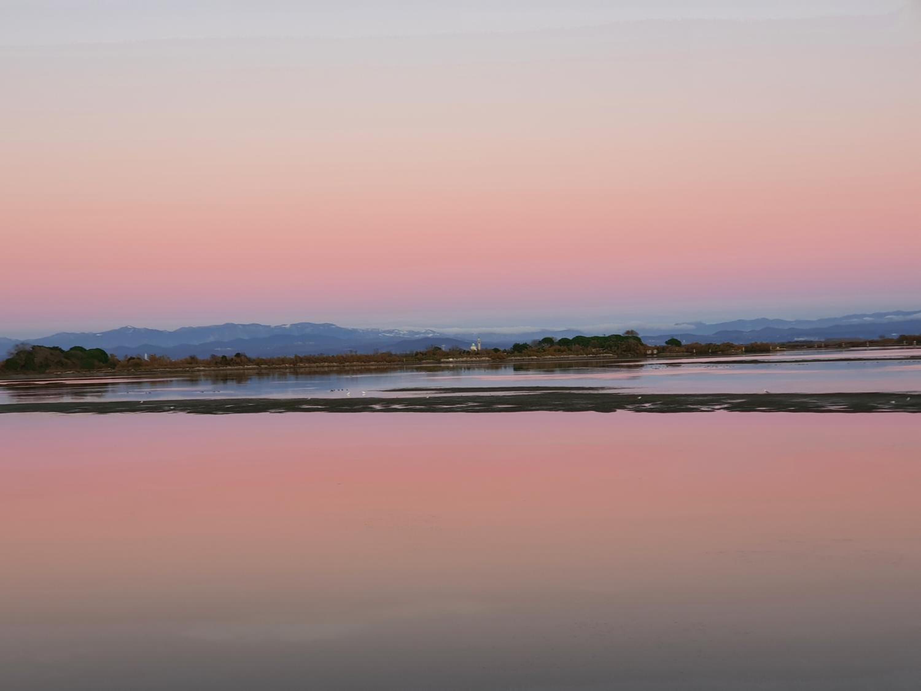 Una vista tranquilla su un lago, con montagne sullo sfondo e un cielo sereno.