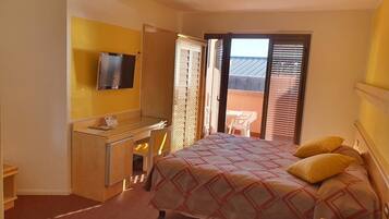 Habitación de hotel con cama, escritorio con televisor, una mesita pequeña y puerta corrediza a un espacio exterior.