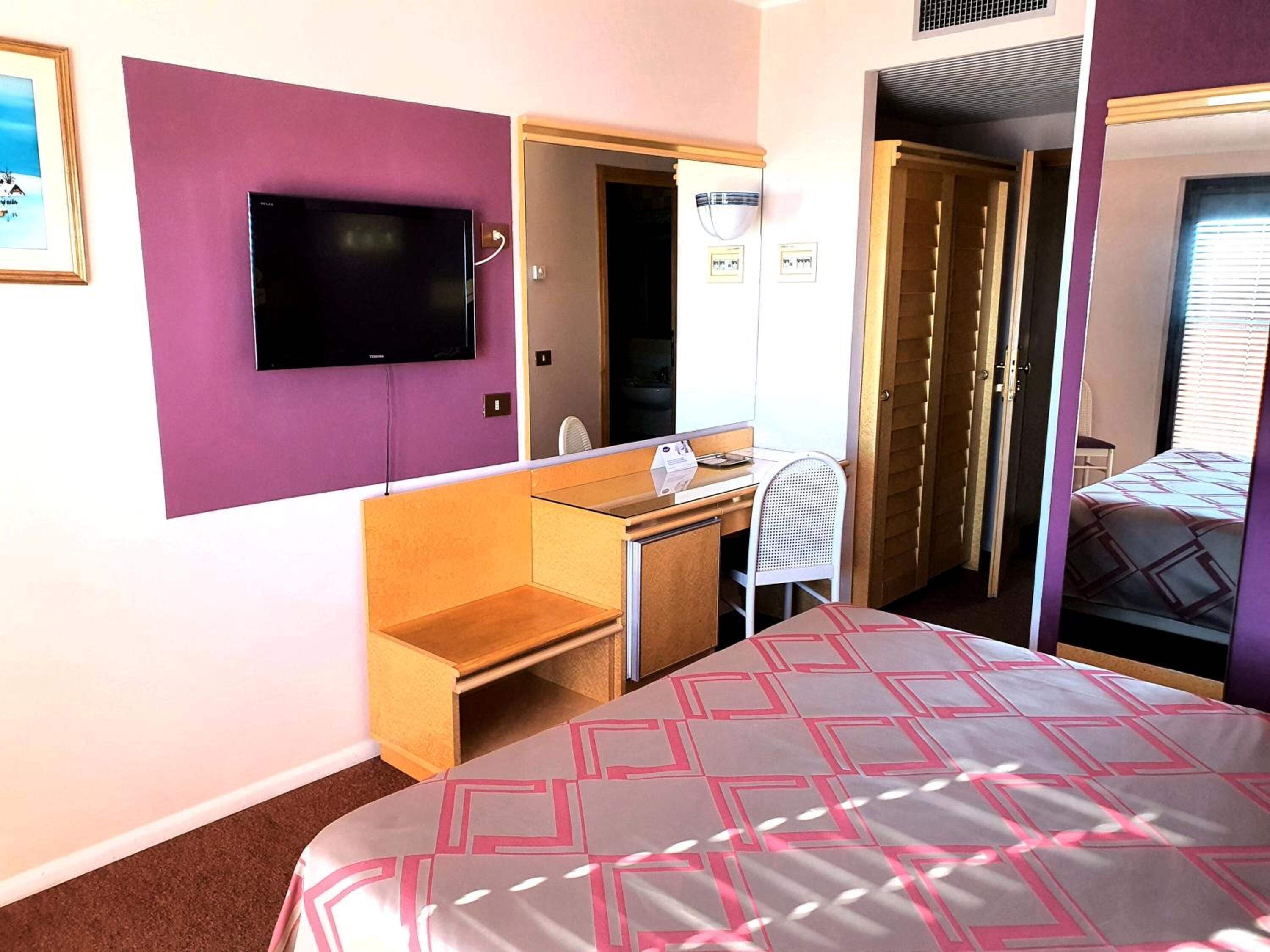 A hotel room with a bed, a desk, a chair, a television, and a bathroom door.