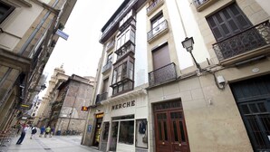 A street view with a building labeled 'MERCHE' featuring a shop window with clothing items and a closed shop door. - Dream | The Rentals Collection (San Sebastián/Donostia)
