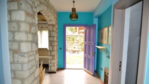 Un couloir avec un mur en pierre, une porte bleue et un sol carrelé qui mène à un espace extérieur.