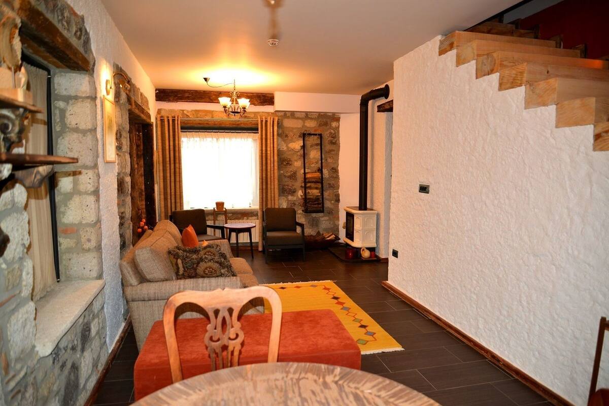Una sala de estar acogedora con chimenea de piedra, una escalera de madera y un comedor con mesa y sillas.