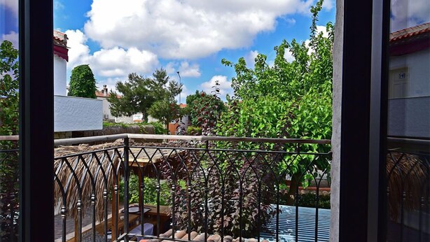Un balcon donnant sur un jardin, une pergola et un ciel d’un bleu éclatant.