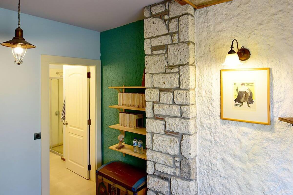 Una habitación con techo de madera, pared de piedra, cama, estante con libros y un cuadro enmarcado.