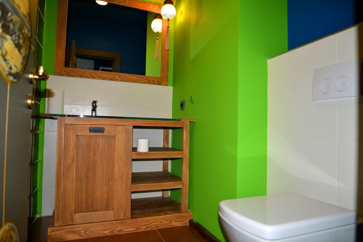A bathroom with a wooden vanity, a toilet, and a green wall.