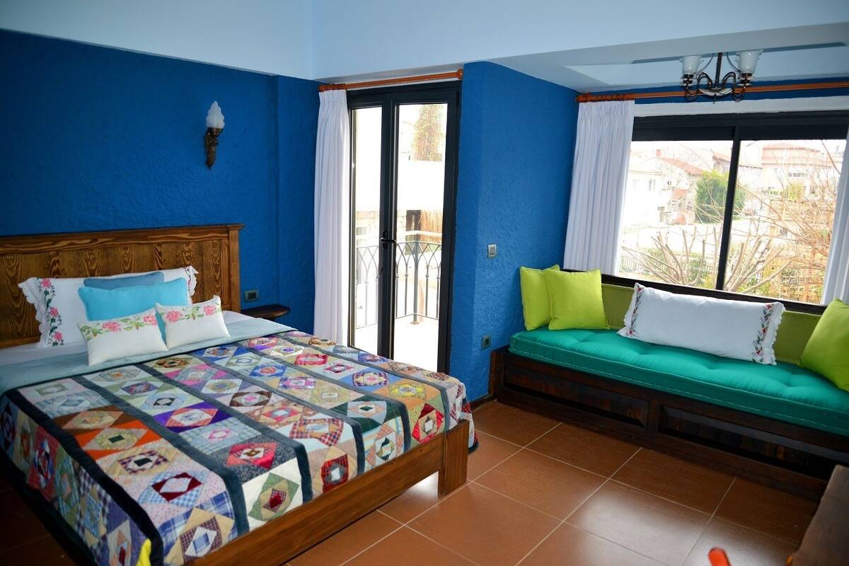 Un dormitorio con una cama de madera, un sofá verde y vistas al exterior.