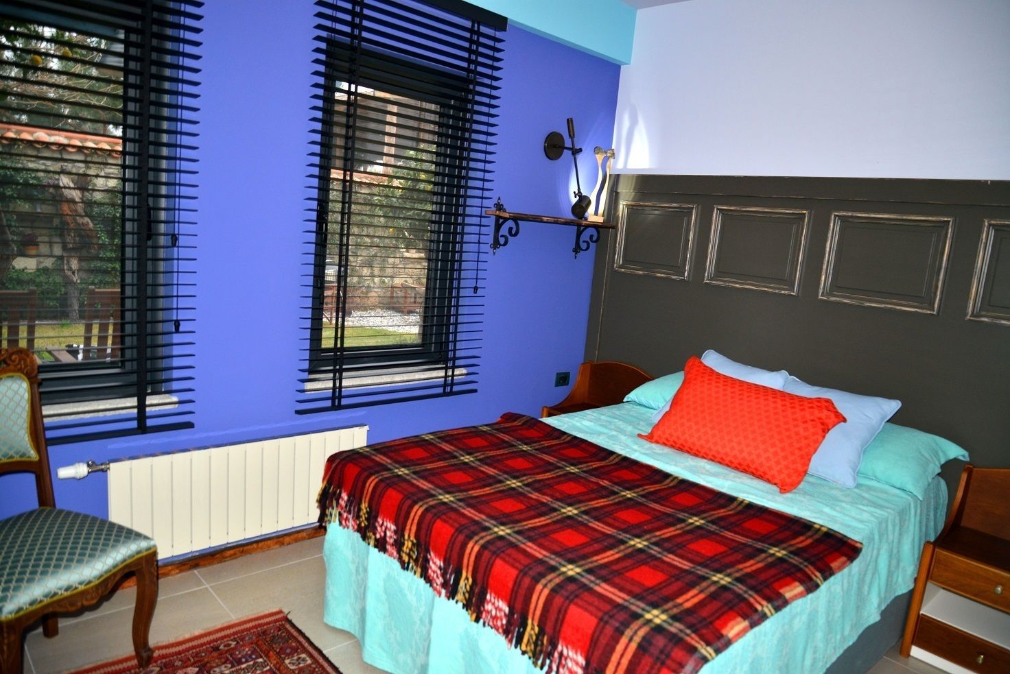 A bedroom with a bed, a chair, a window with blinds, and a radiator.