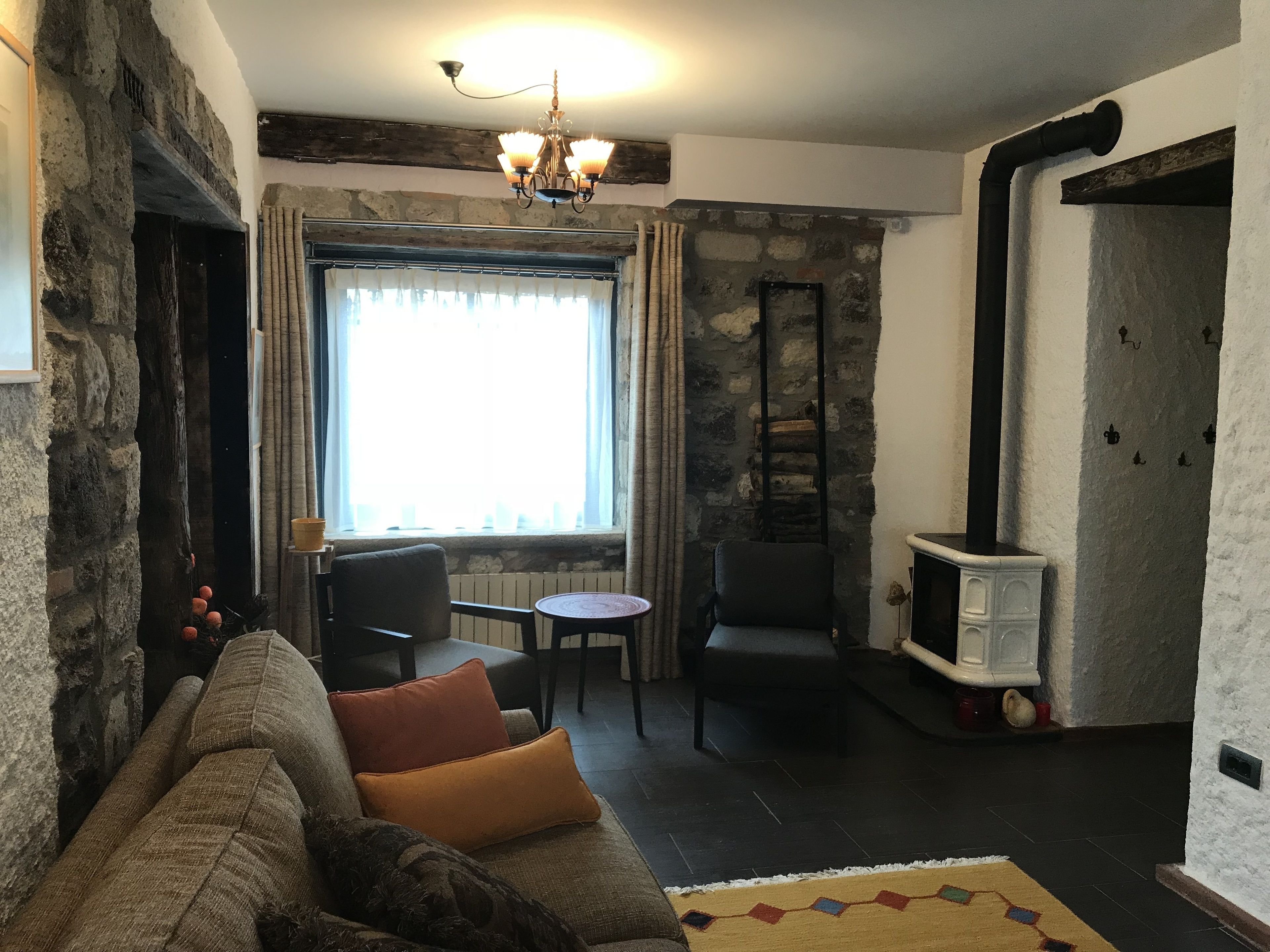 Un salon chaleureux avec un mur en pierre, une cheminée, un canapé avec des coussins, une table à manger et un lustre.