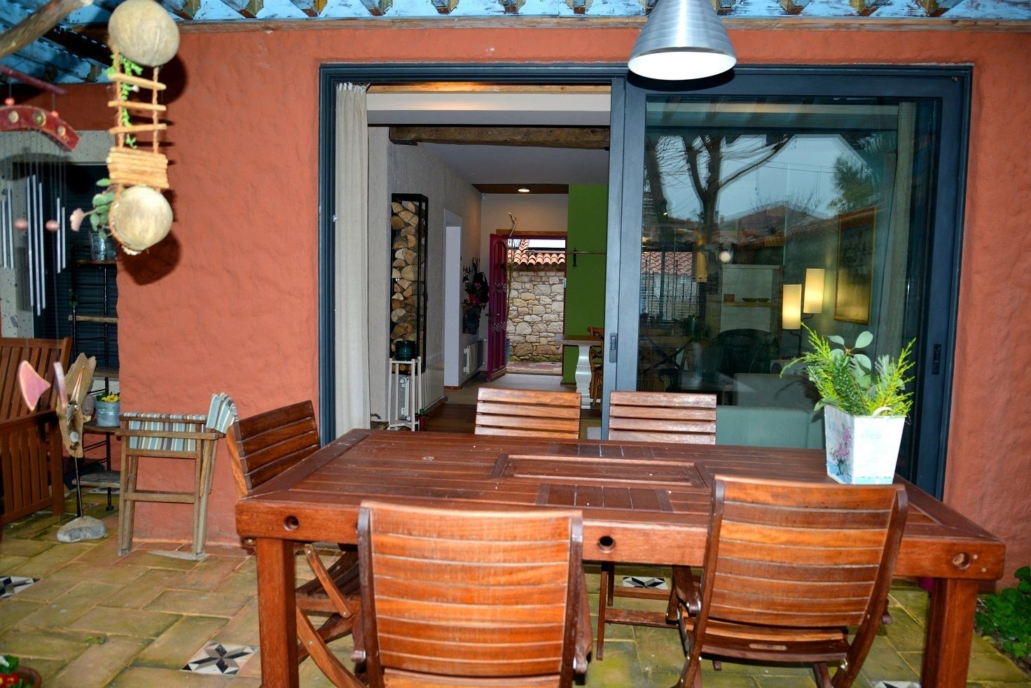 An outdoor dining area with a wooden table and chairs, a hanging decoration, and a potted plant.