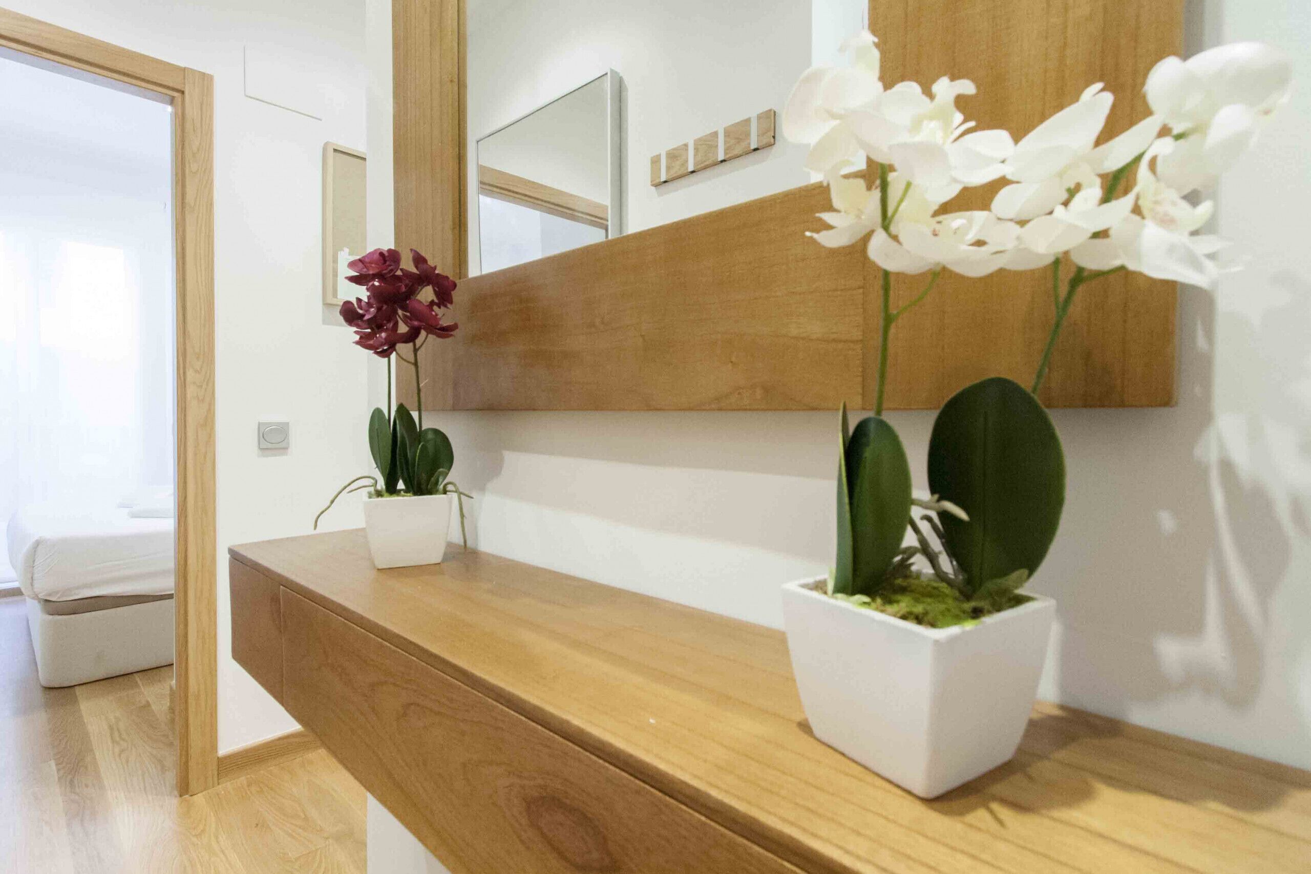Una consola de madera con dos plantas en macetas, una con flores blancas y otra con hojas verdes.