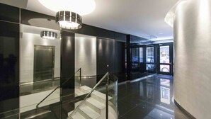A modern lobby with a glass staircase, a ceiling light fixture, and a view of the outside through glass doors.