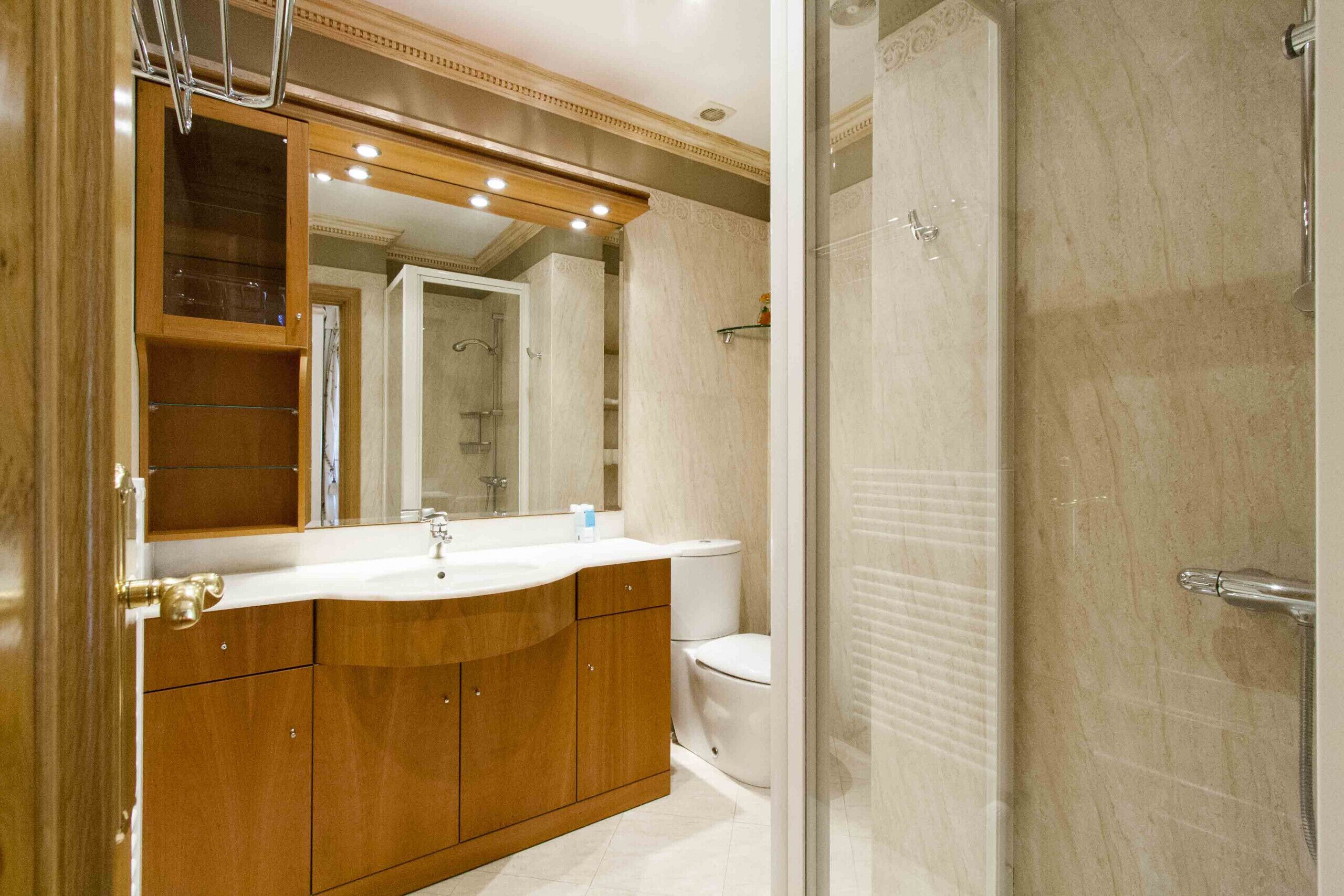 A bathroom with a wooden vanity, a sink, a mirror, and a shower enclosure.