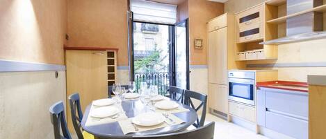 A dining area with a round table set for four, a kitchen with modern appliances, and a view through an open door.