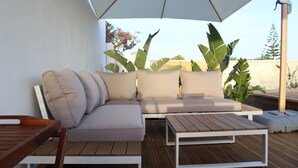 Eine Holzterrasse mit einer weißen Couch und einem Tisch unter einem großen Sonnenschirm.