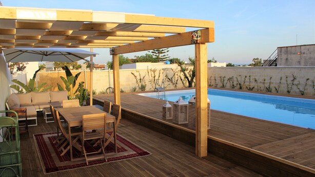 Eine Holzterrasse mit Pool, Gartenmöbeln und einer Pergola, die Schatten spendet.