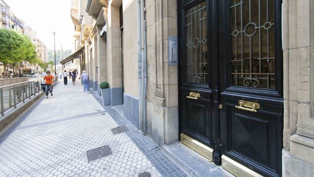 A sidewalk leading to a building with a black ornate door and a metal gate. - Gallery | The Rentals Collection (San Sebastián/Donostia)
