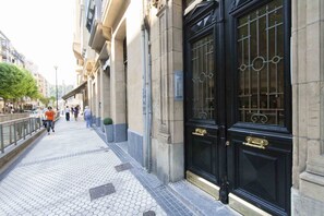 Una acera que condueix a un edifici amb una porta negra i ornamentada i una reixa metàl·lica.
