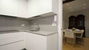 A modern kitchen with white cabinets, a sink, and a dining area with a table and chairs. - Gallery | The Rentals Collection (San Sebastián/Donostia)