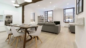 A modern kitchen with white cabinets, a built-in oven, and a dining area with a wooden table and white chairs.