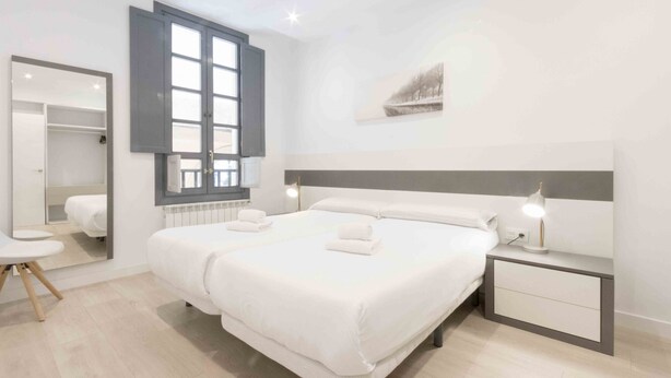 A modern hotel room with a large bed, bedside tables, a mirror, and a window.