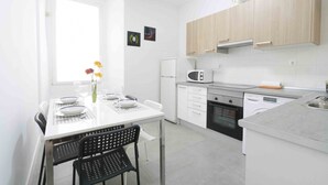 A modern kitchen with white cabinets, a microwave, a dishwasher, and a dining area with a table and chairs. - Coeur | The Rentals Collection (San Sebastián)