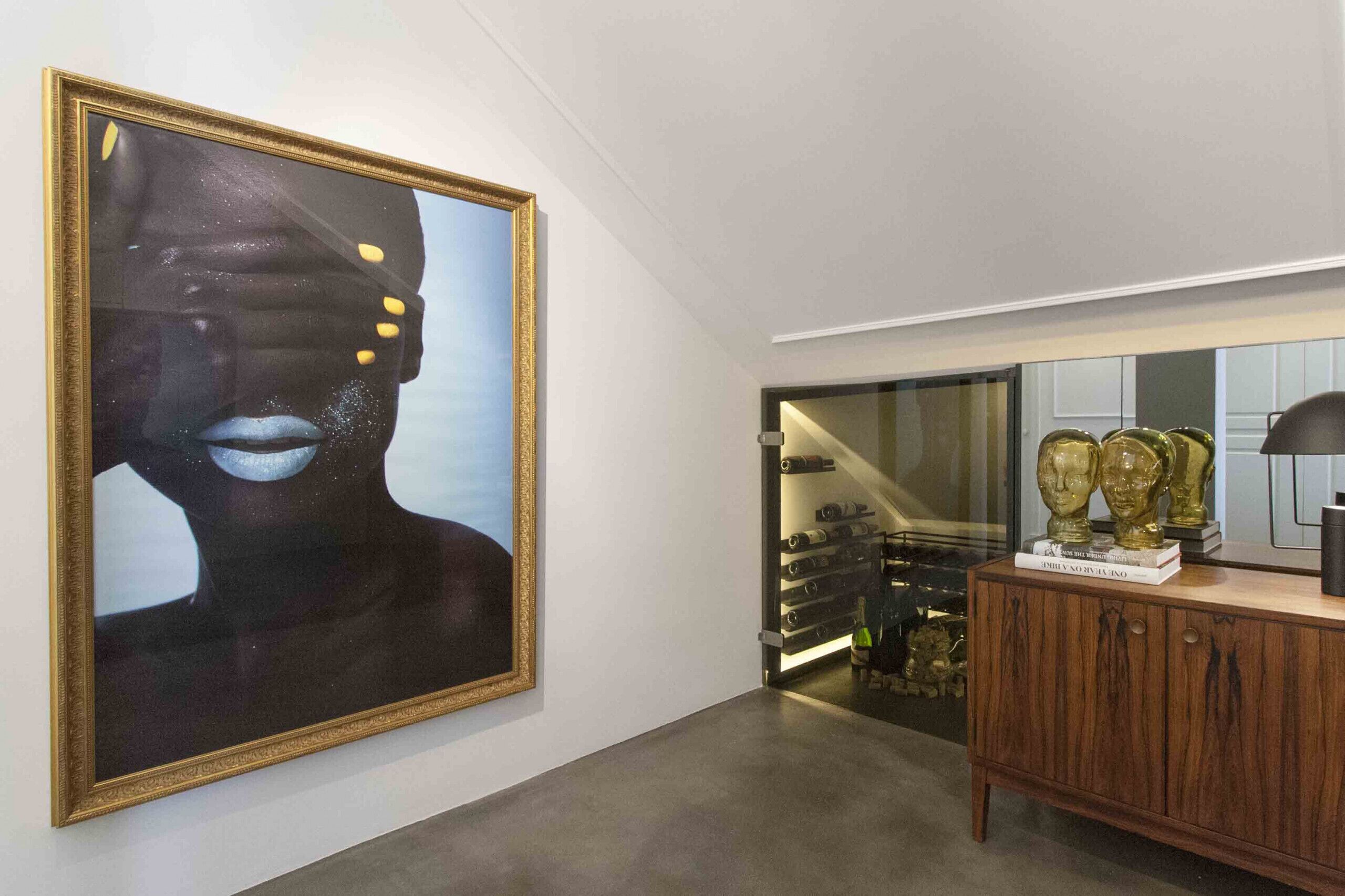 A modern interior with a large abstract painting, a wine rack, and decorative busts on a wooden cabinet.