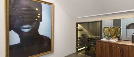 A modern interior with a large abstract painting, a wine rack, and decorative busts on a wooden cabinet.