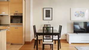 A dining area with a table and chairs, a kitchen with appliances, and a TV on a stand.