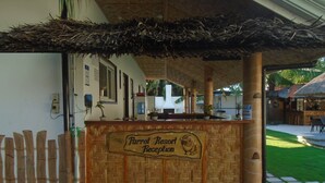 Un espace d’accueil avec une enseigne en bois indiquant « Réception du Parrot Resort » et un toit de chaume au-dessus.