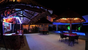 Un espace bar extérieur doté de parasols en chaume, de sièges et situé au bord de la piscine.