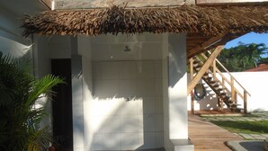 Une douche extérieure abritée, dotée d’un toit de chaume, de murs recouverts de carreaux blancs et d’une terrasse en bois.