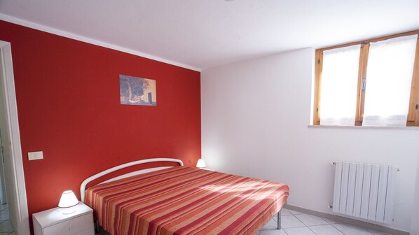 Un dormitorio con cama, mesita de noche, ventana y radiador.