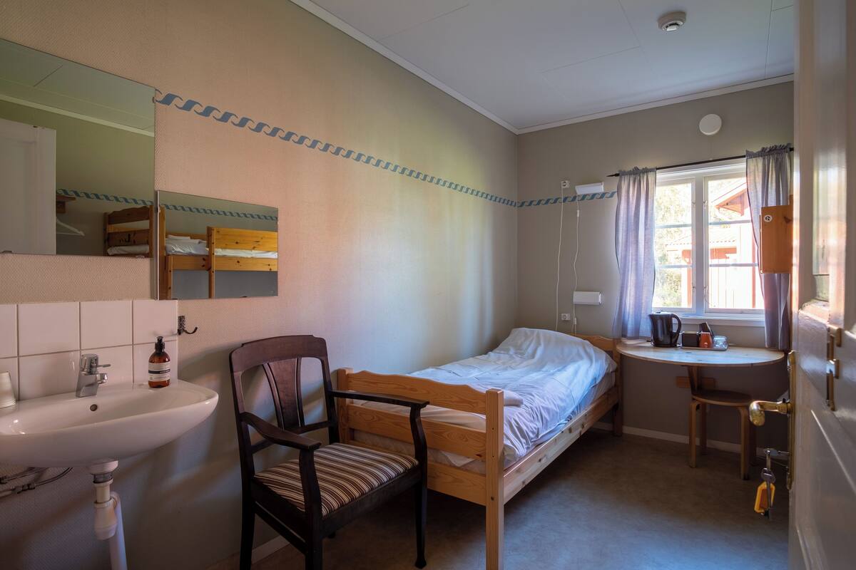 Un dormitorio compacto con una cama individual, un escritorio pequeño, una silla, un lavamanos y un espejo.