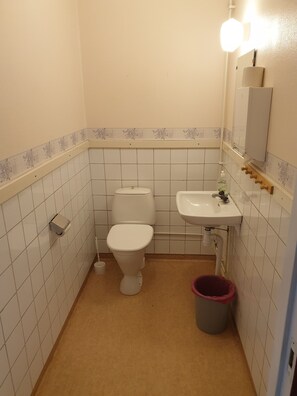 Un baño pequeño con inodoro, lavamanos y un cubo de basura.