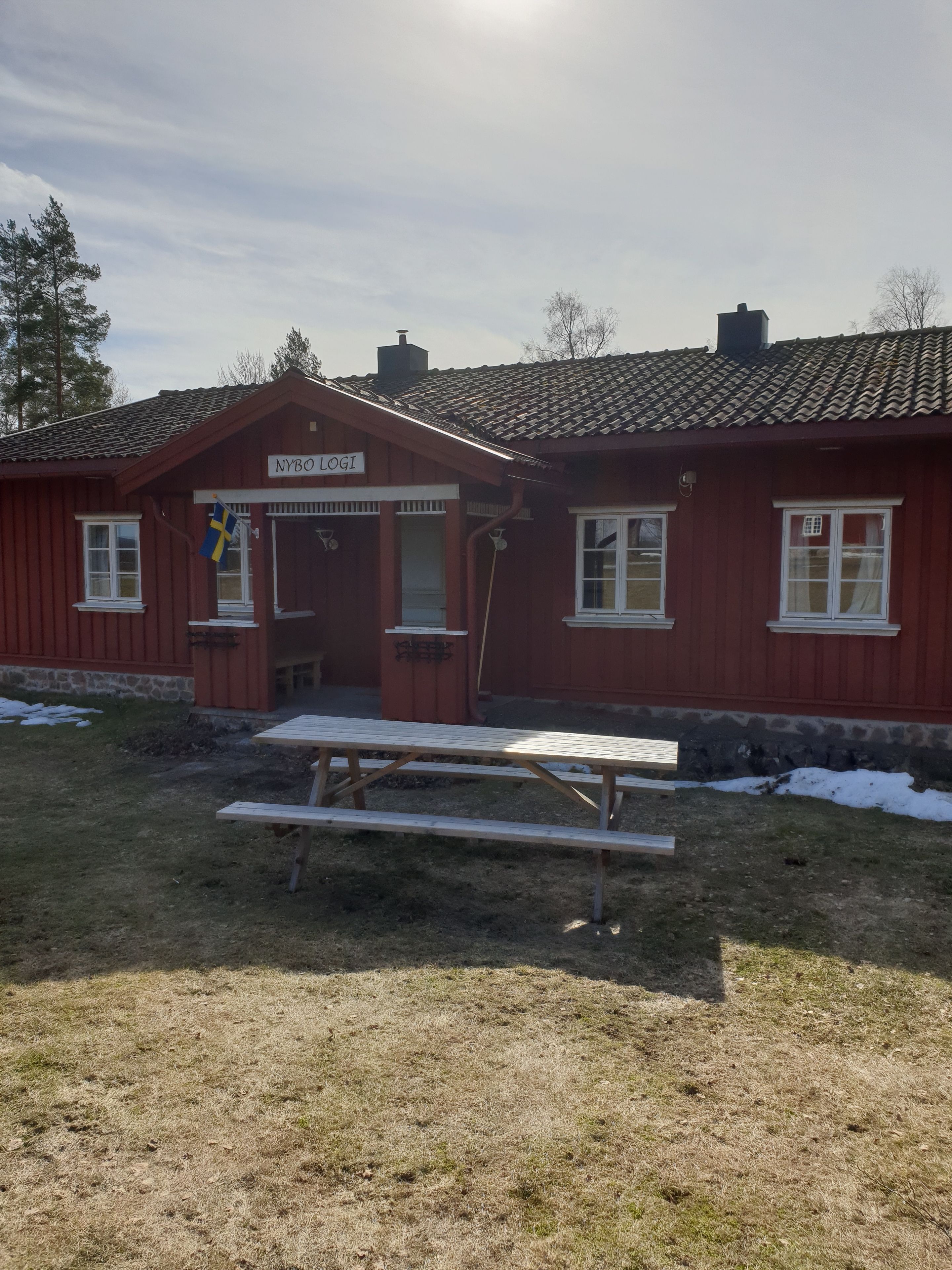 A red wooden building with a sign reading "NYBO LOGI".