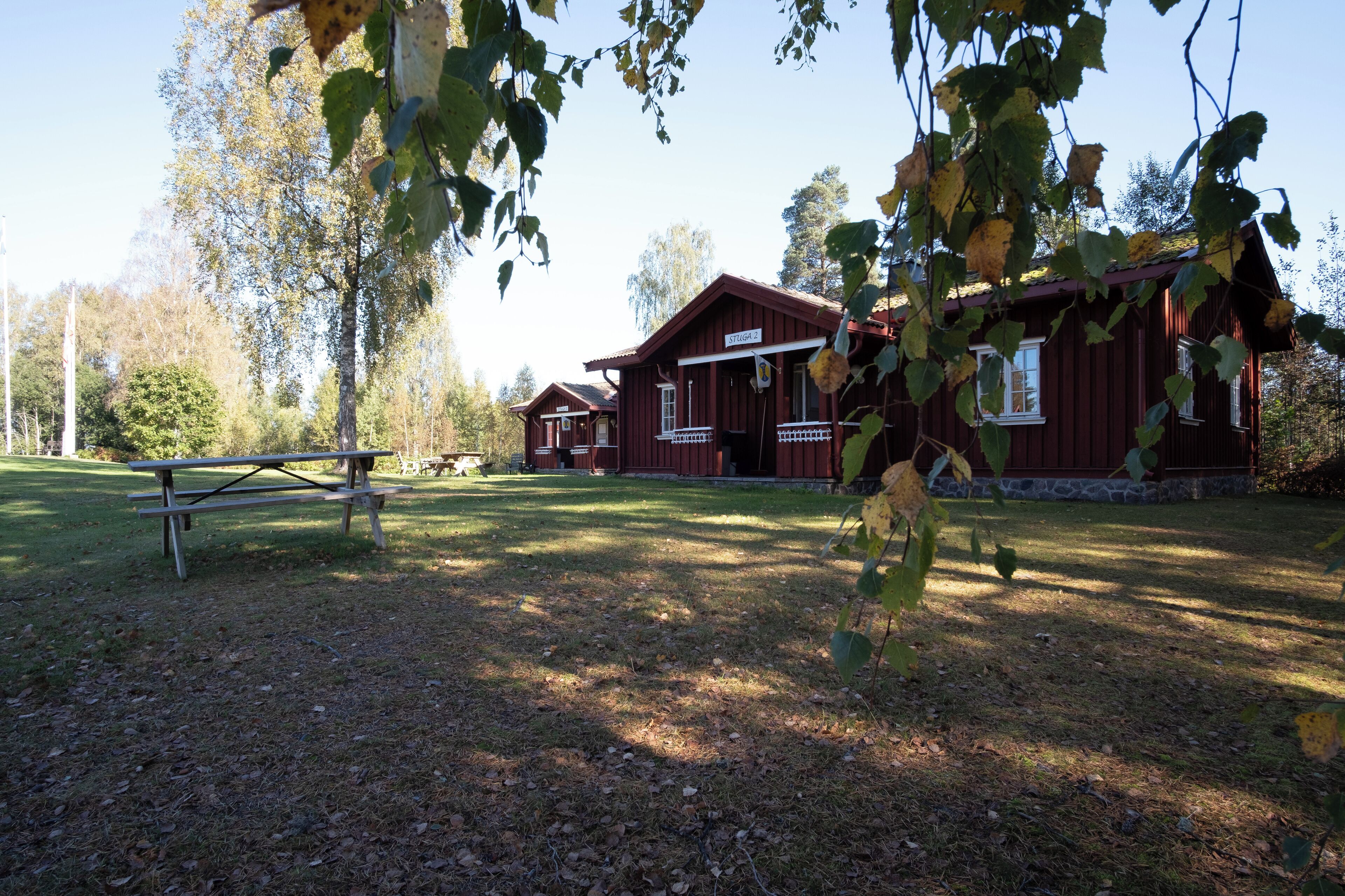 A rustic cabin with a porch and a picnic table in a wooded area.