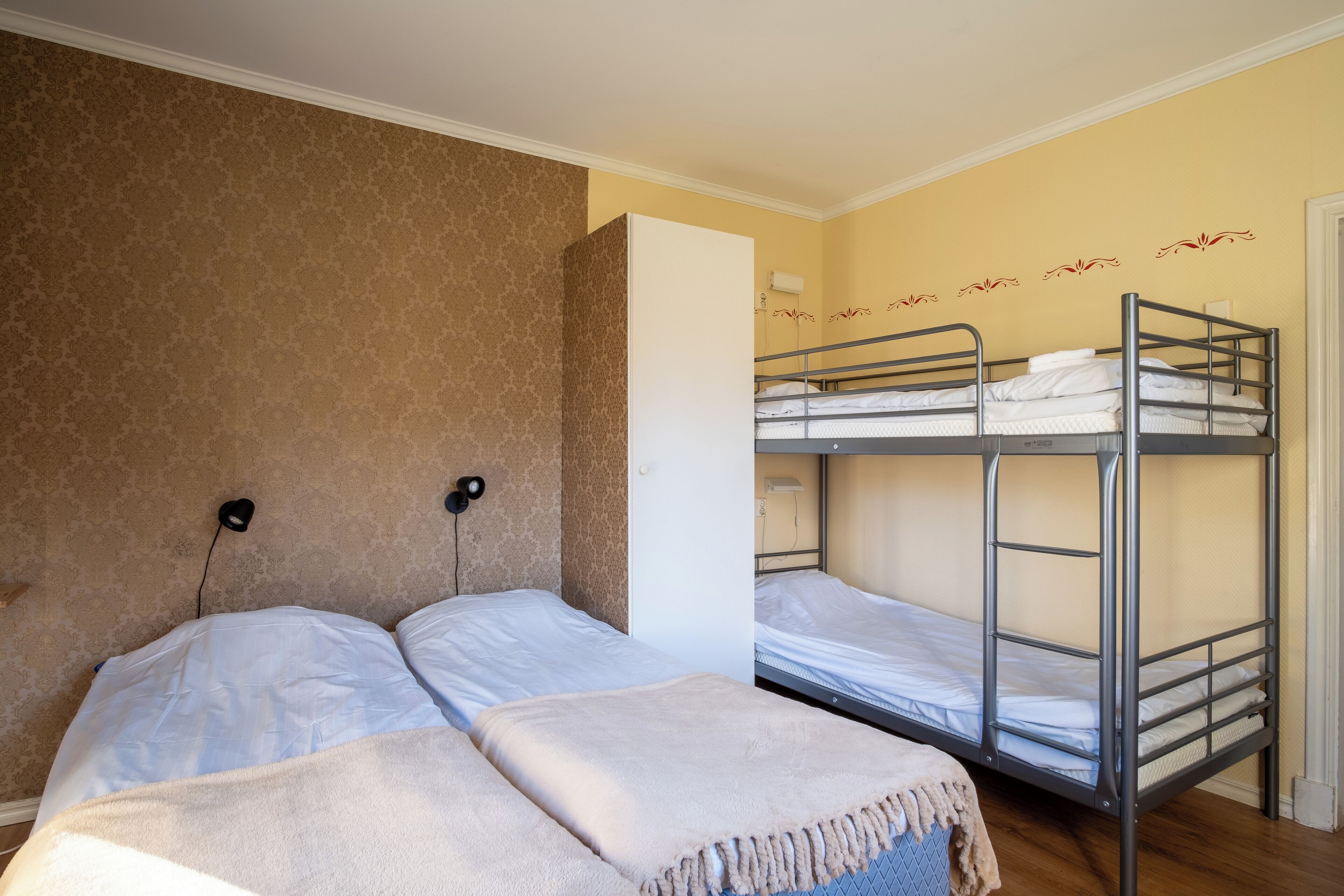 Een kamer met twee eenpersoonsbedden en een stapelbed, voorzien van nachtlampjes en een behang met patroon.