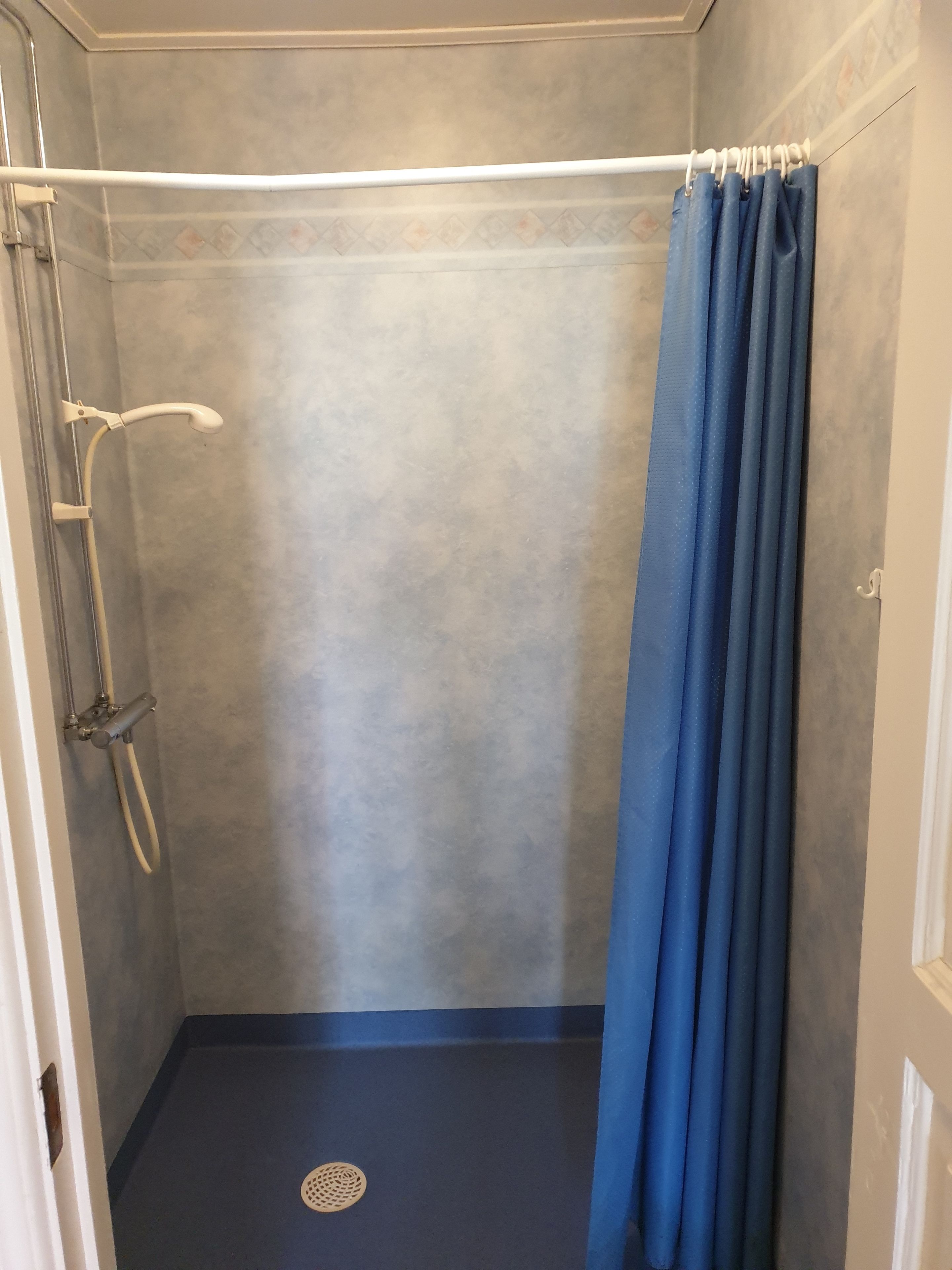 A small, enclosed shower area with a blue curtain, a handheld showerhead, and a drain.