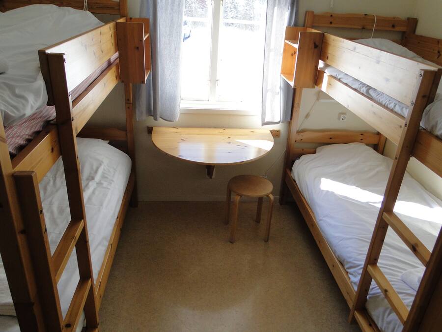 Quarto com beliche, uma pequena mesa de madeira e um banquinho.