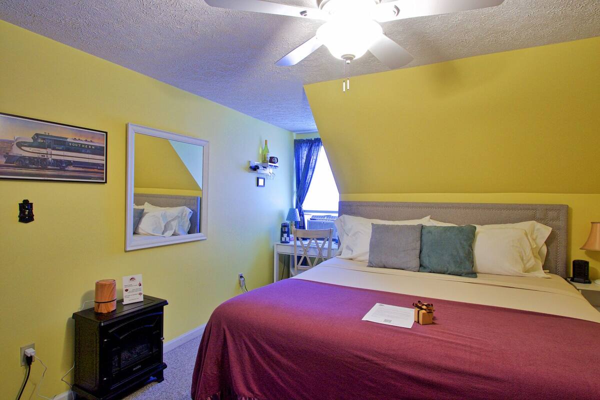 A bedroom with a bed, a ceiling fan, a nightstand, a lamp, a mirror, and a framed picture on the wall.
