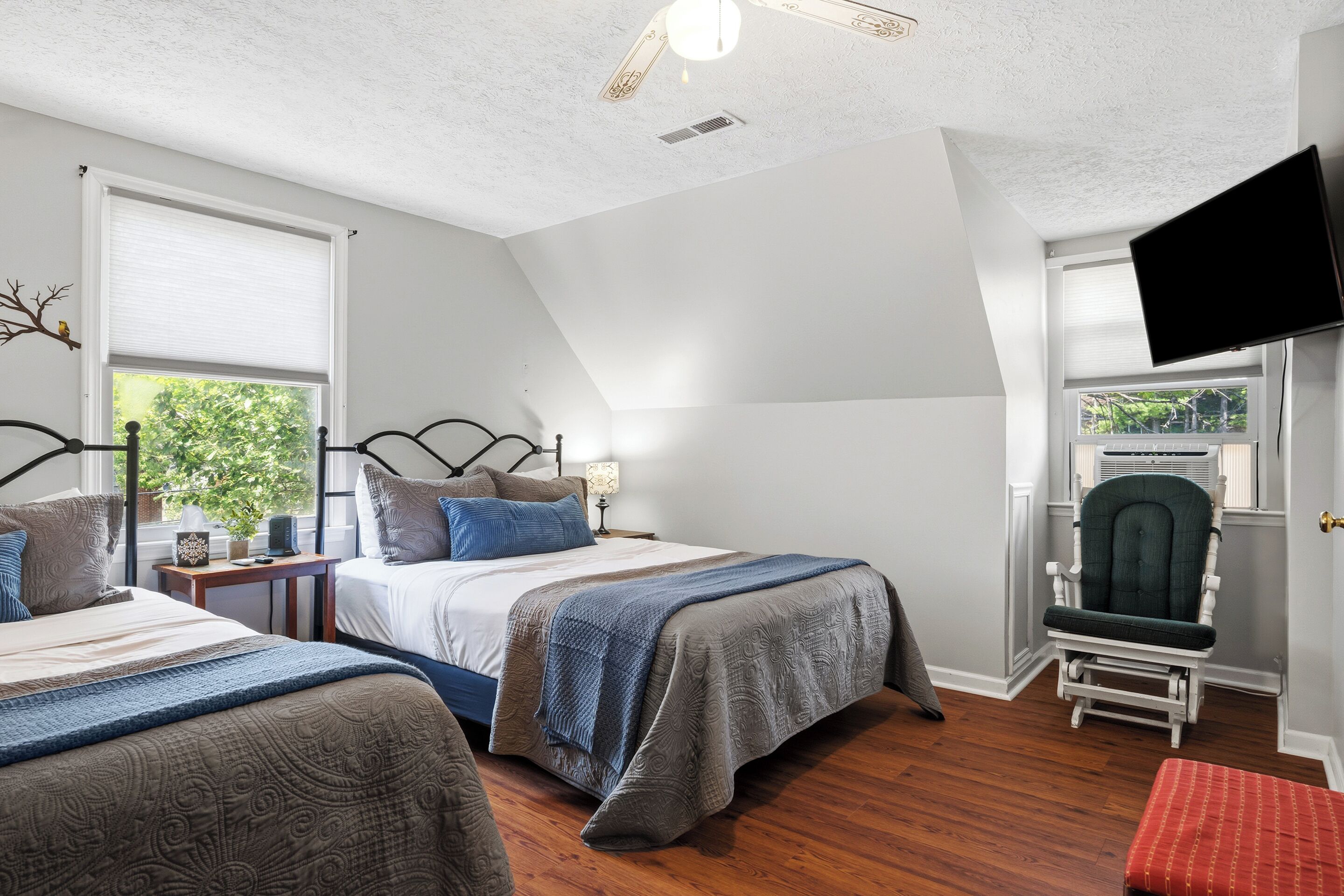 A bedroom with two beds, a television, a chair, and a window with blinds.