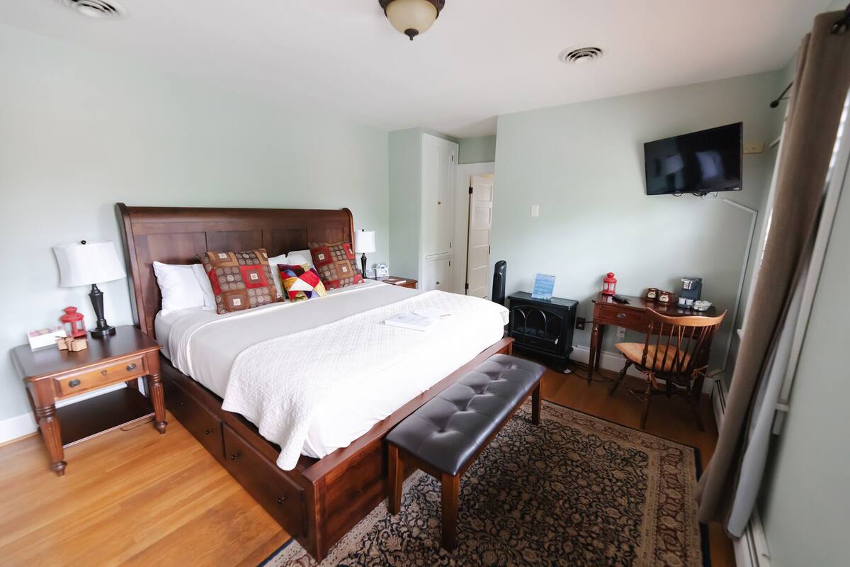 A neatly arranged bedroom with a wooden bed, bedside tables, a desk, and a television.