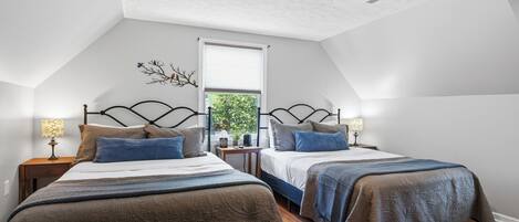 A bedroom with two beds, a ceiling fan, a window with a view, and a nightstand with a lamp.