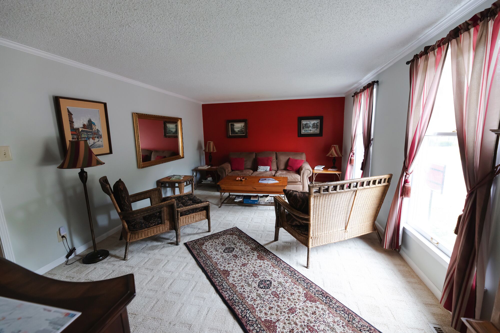 A living room with a red accent wall, a sofa, a coffee table, and wicker furniture.