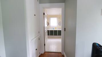 A narrow hallway leading to a kitchen with white cabinets, a window, and a tiled floor.