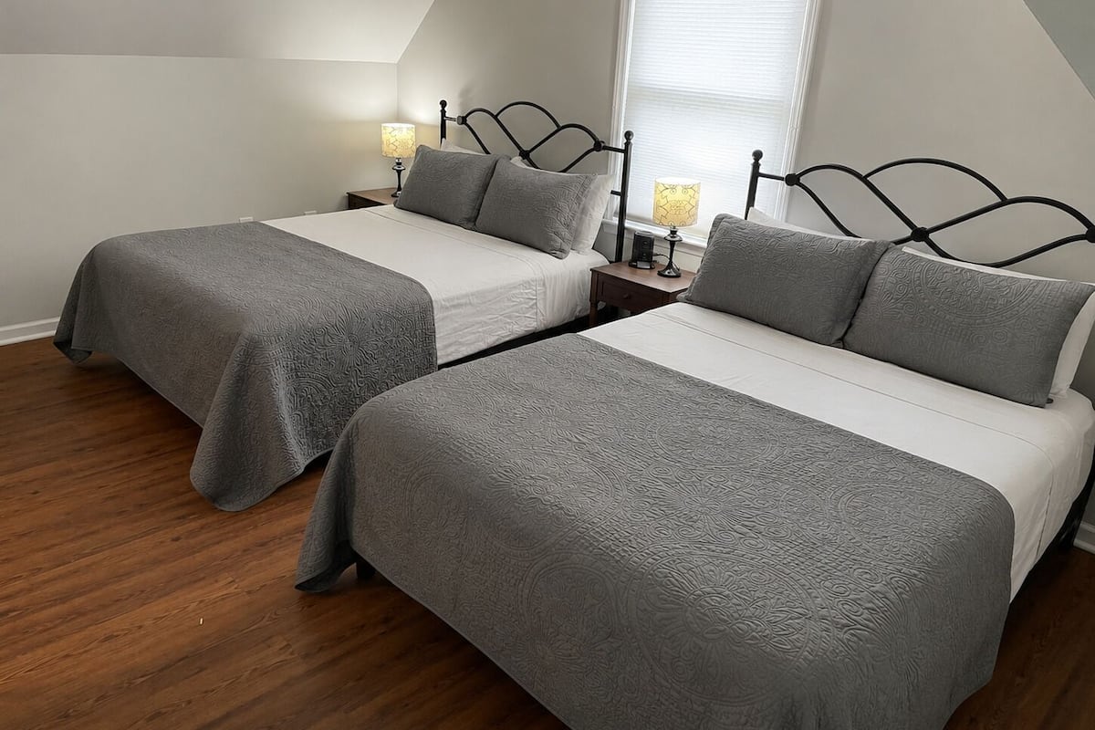 A bedroom with two beds, wooden flooring, and a window with blinds.