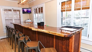 Een bar met een houten toonbank, barstoelen, een televisie en een raam met luiken.