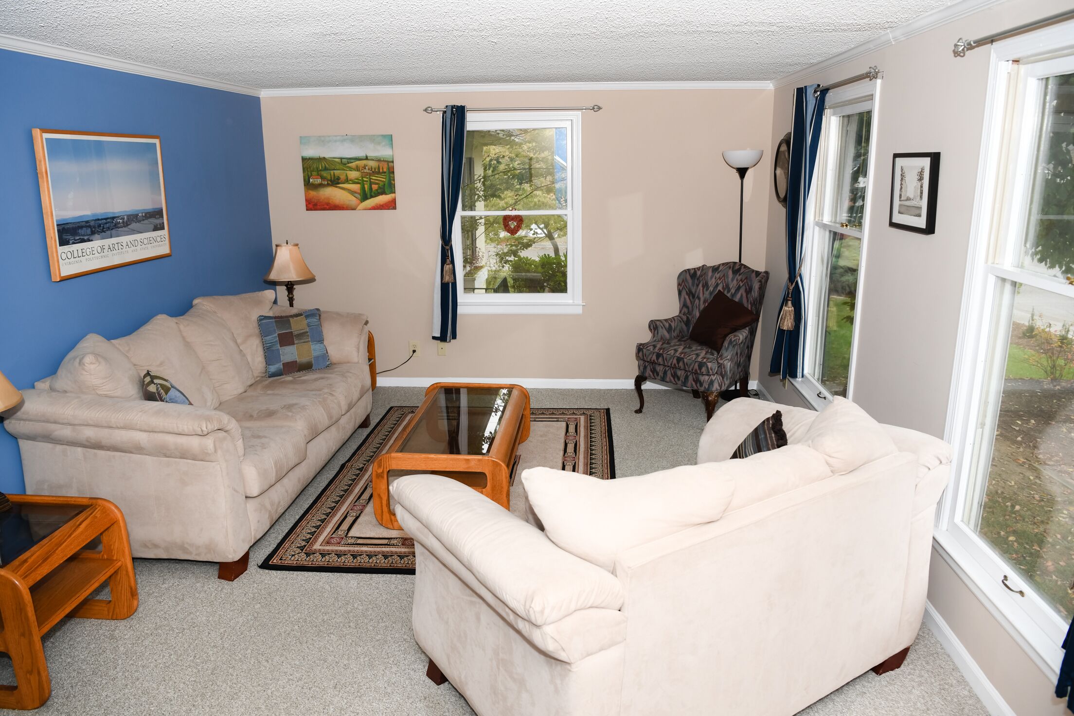A living room with a beige sofa, a patterned armchair, a glass coffee table, and a rug.